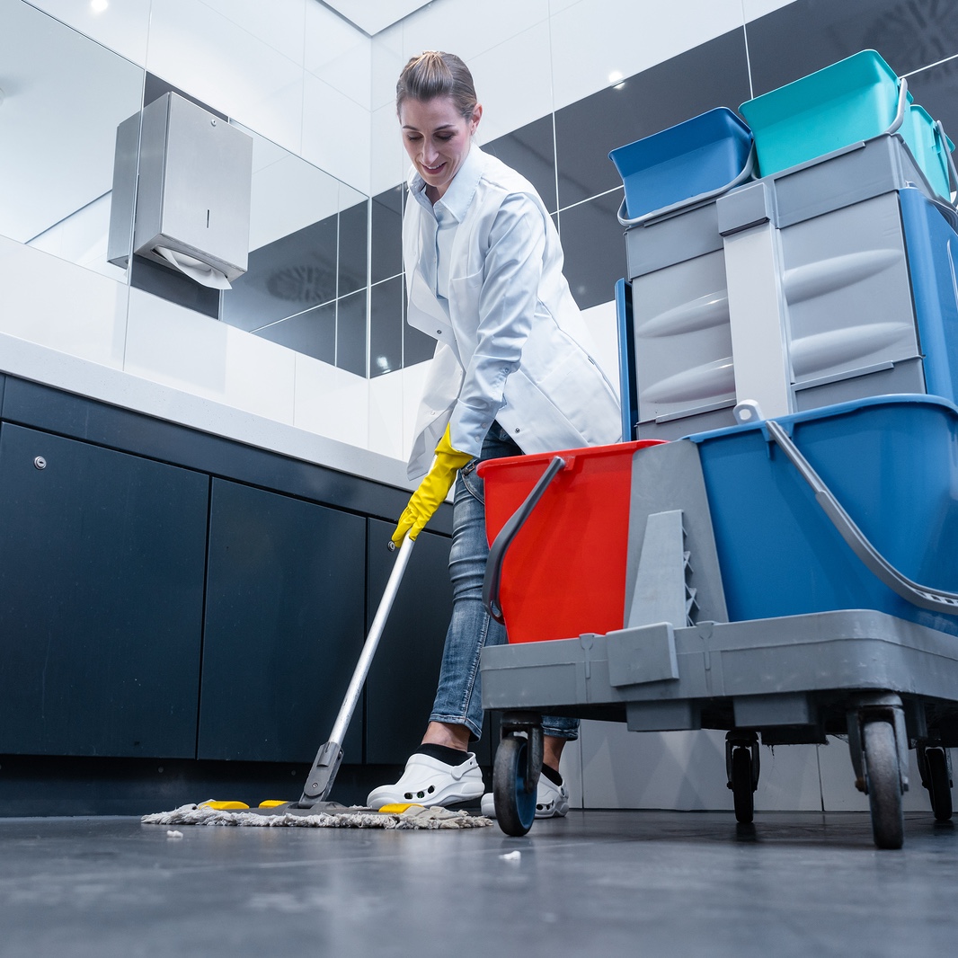 Cleaning lady mopping the floor in restroom cleaning the toilet